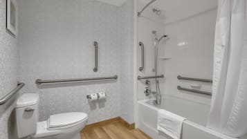 A bathroom with a toilet, a shower, and handrails.
