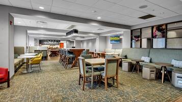 A hotel lobby with multiple seating areas, including tables and sofas, carpeted flooring, and a ceiling with recessed lighting.