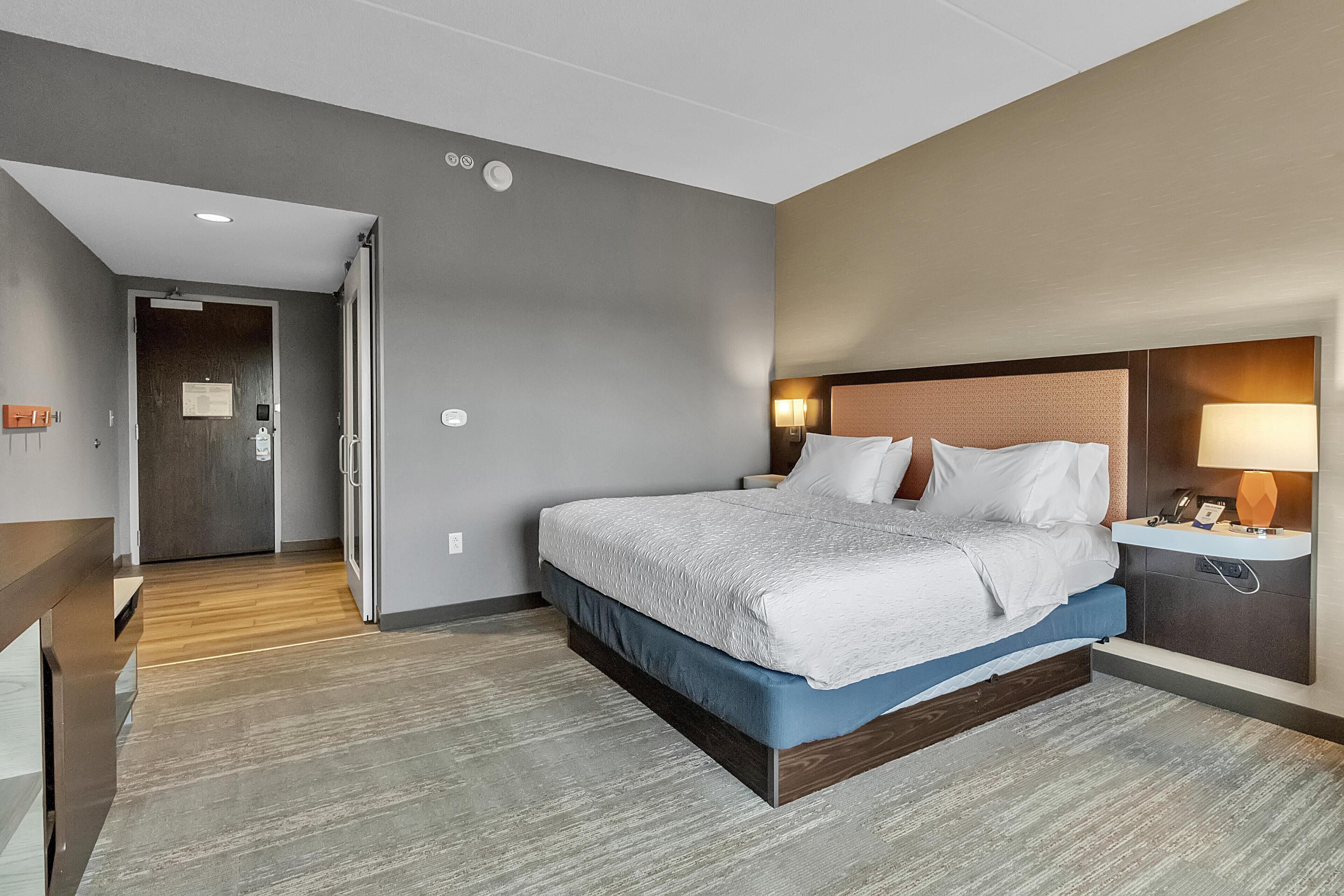A hotel room with a large bed, a bedside table with a lamp, and a wooden floor.