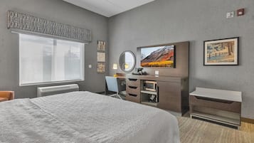 Una habitación de hotel con una cama grande, un escritorio con silla, un televisor de pantalla plana, un espejo y una ventana con vista a la ciudad.
