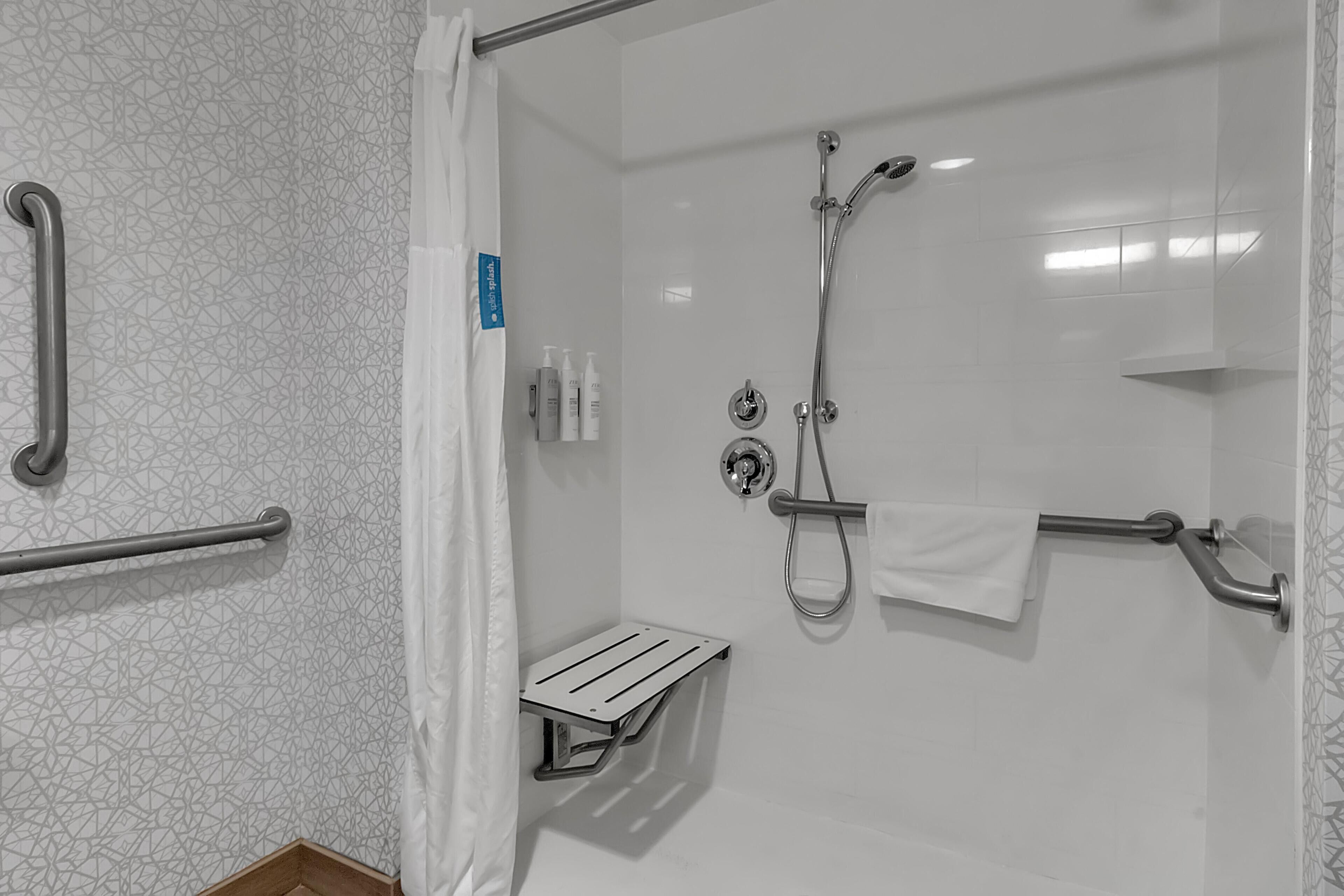 A modern bathroom with a walk-in shower, grab bars, a towel rack, and a small shelf.