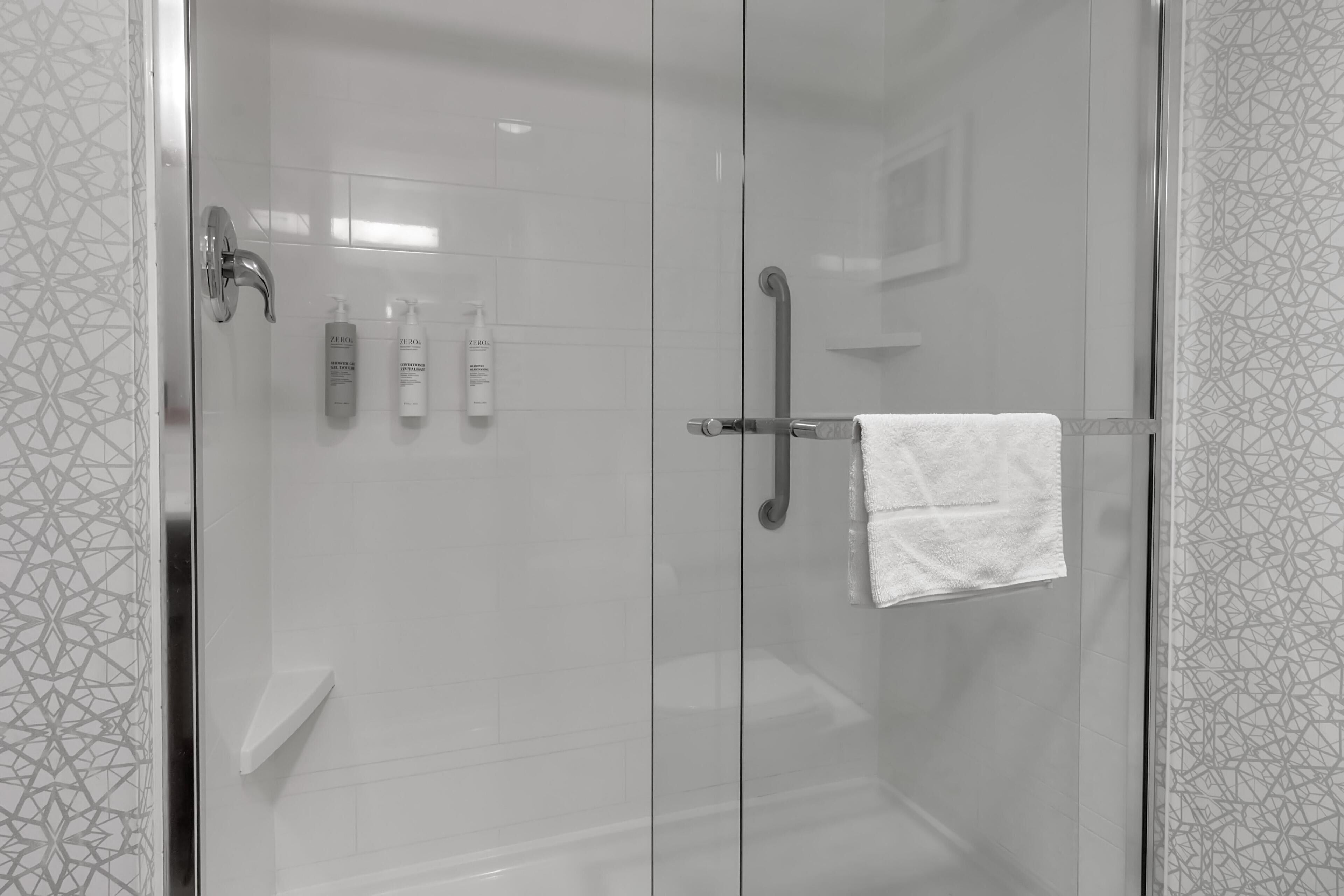 A modern shower area with glass doors, a handrail, and a white towel hanging on the door.