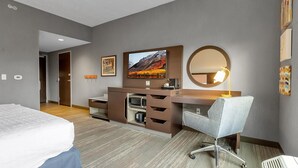 A modern hotel room with a bed, a desk with a chair, a flat-screen TV, a microwave, and a large mirror. - Hampton Inn Buffalo - Amherst, NY (Buffalo)