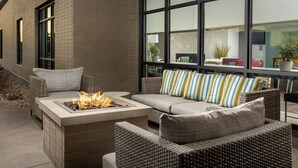 A modern outdoor seating area with a fire feature, wicker furniture, and large windows offering views of the interior. - Home2 Suites by Hilton Denver Central Park (Denver)