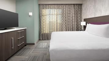 Een hotelkamer met een groot bed, een flatscreen televisie op een houten dressoir, een nachtkastje met een lamp en een gordijn met dessin.