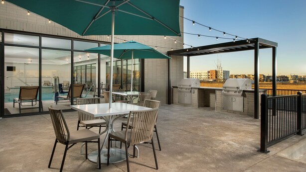 An outdoor patio with tables and chairs, a barbecue grill, and a view of the city skyline. - Home2 Suites by Hilton Denver Central Park (Denver)