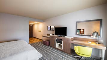 Una habitación de hotel con cama, escritorio, silla, televisor y espejo.