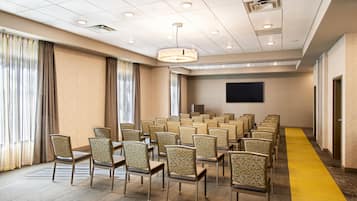 A conference room with rows of chairs, a large screen, and a carpeted floor.