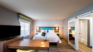Ett hotellrum med en säng, sängbord, ett skrivbord, en stol, en tv och ett badrum som syns genom en öppen dörr.