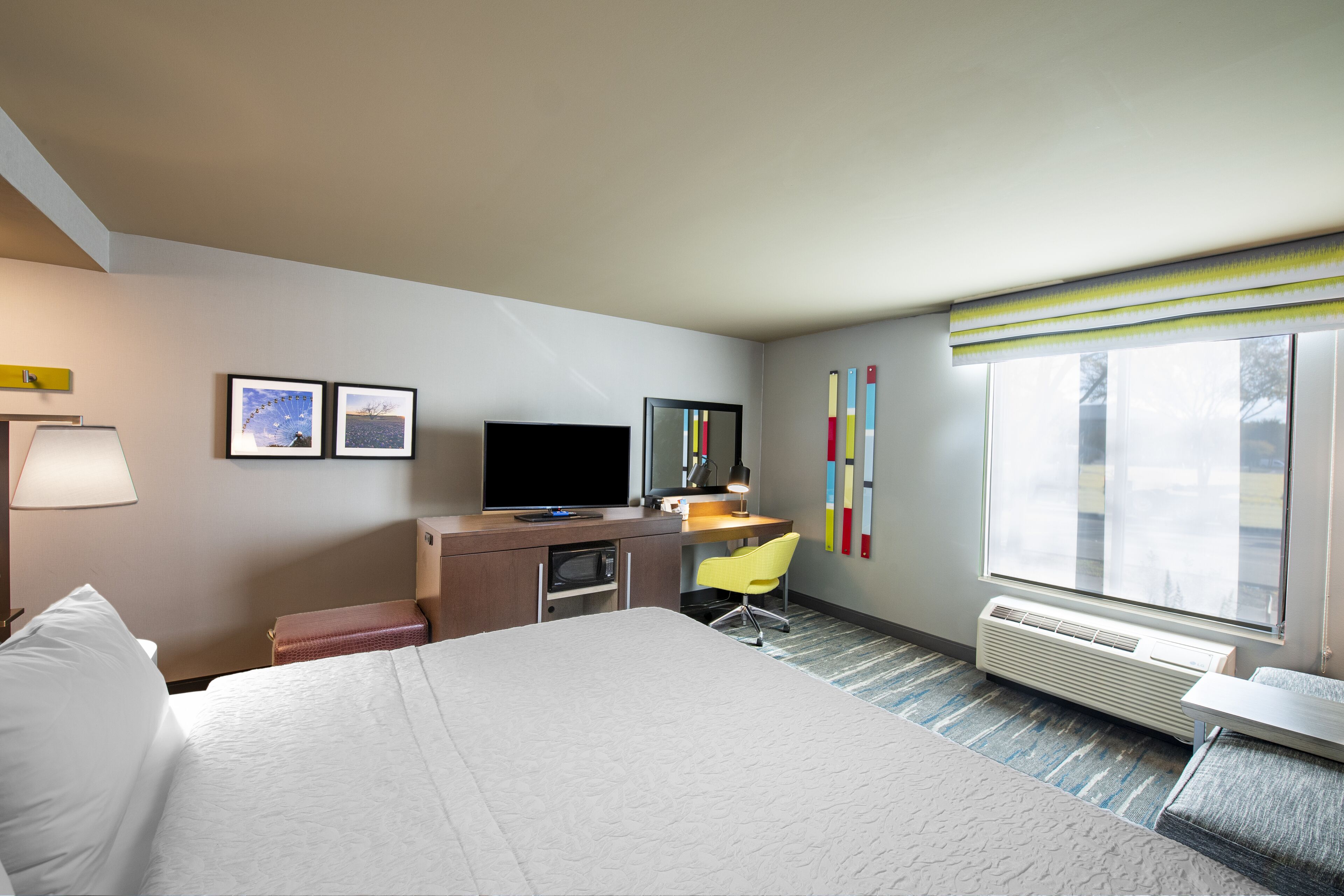 A hotel room with a bed, desk, chair, television, and a window with blinds.