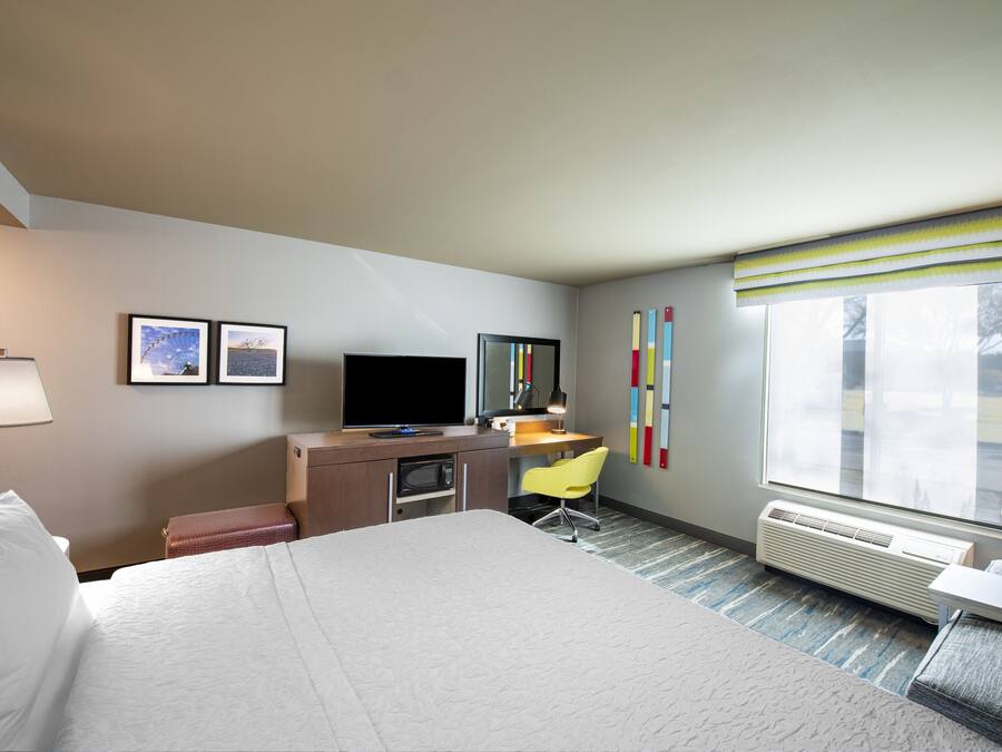 A hotel room with a bed, desk, chair, television, and a window with blinds.