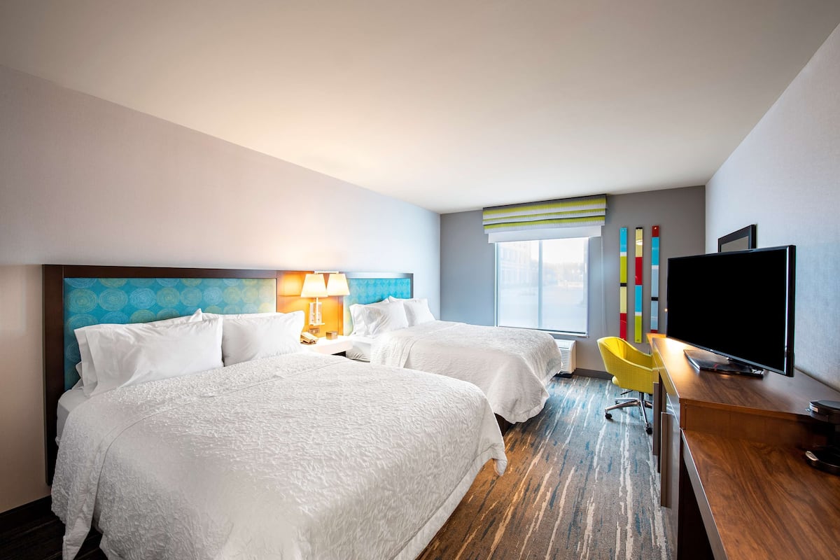 A hotel room with two beds, a desk with a TV, a chair, and a window with blinds.