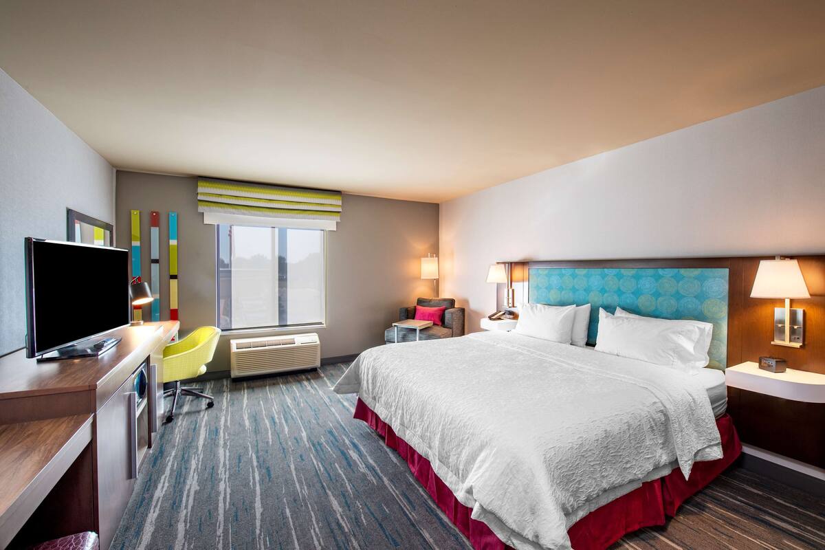 A hotel room with a bed, desk, chair, TV, and window.
