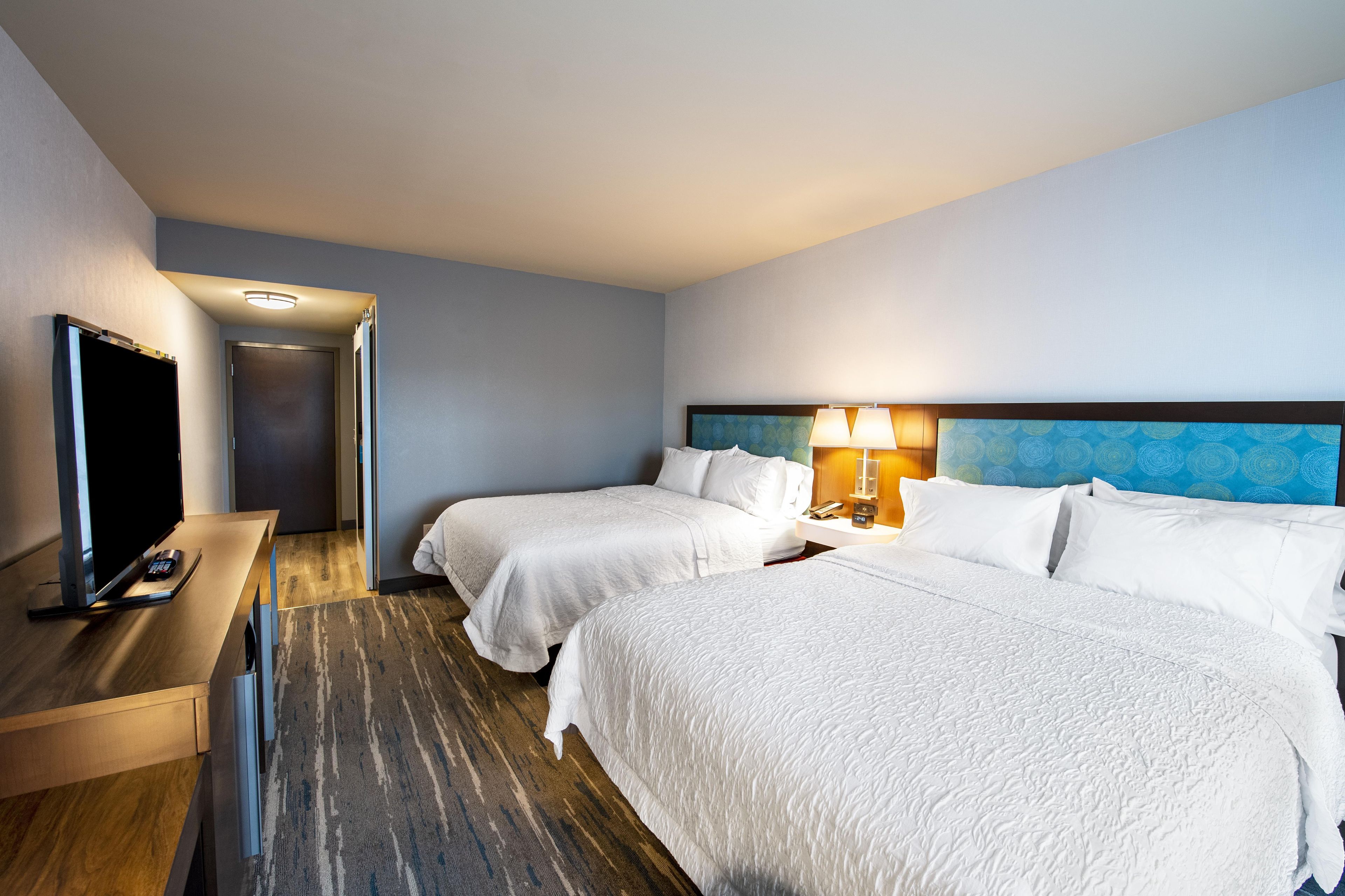 A hotel room with two beds, a TV, and a desk.