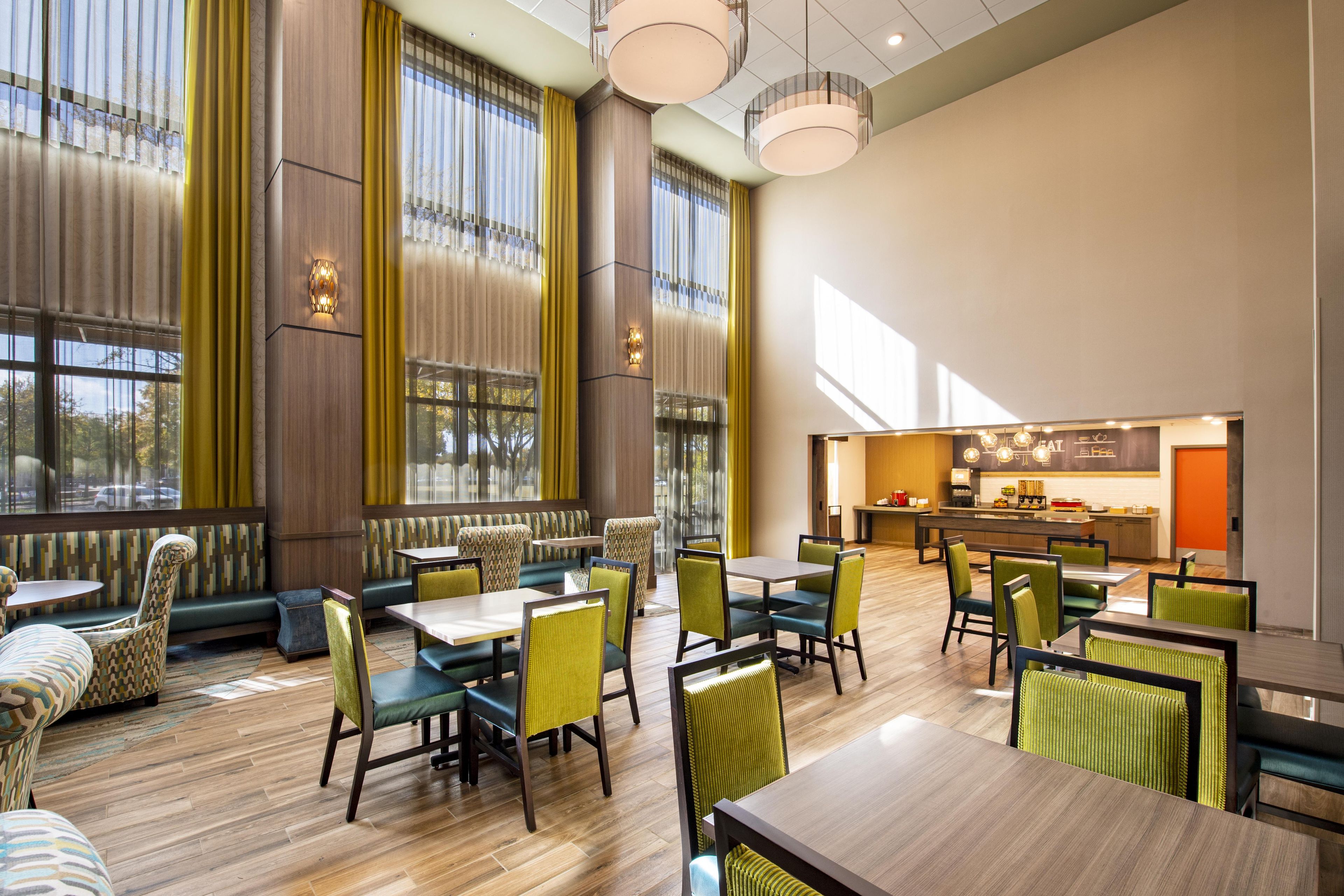 A spacious dining area with high ceilings, large windows, and a modern kitchen visible in the background.