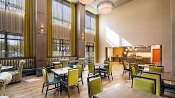 A spacious dining area with high ceilings, large windows, and a modern kitchen visible in the background.