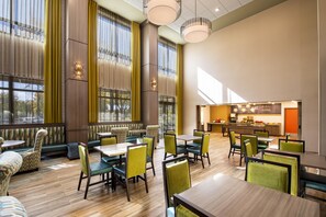 A spacious dining area with high ceilings, large windows, and a modern kitchen visible in the background.