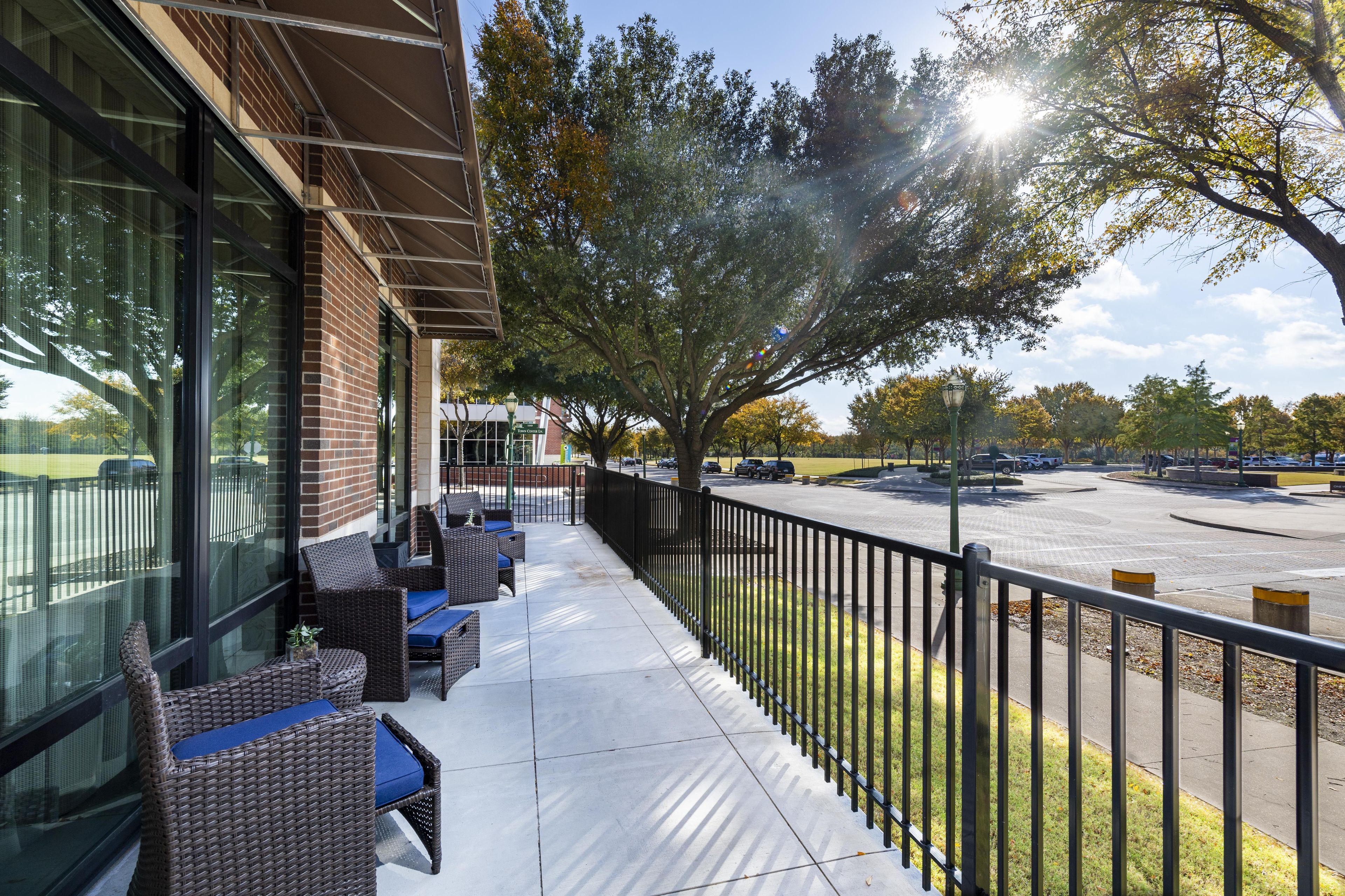 A balcony with wicker furniture, a clear view of a parking lot, and a building with large windows.