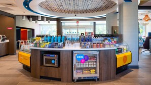 A modern beverage bar with a refrigerated display, a variety of drinks, and a seating area with a view. - Tru By Hilton Eugene, OR (Eugene)