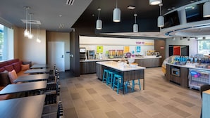 A modern restaurant with a central island, bar seating, and a counter with a beverage display. - Tru By Hilton Eugene, OR (Eugene)