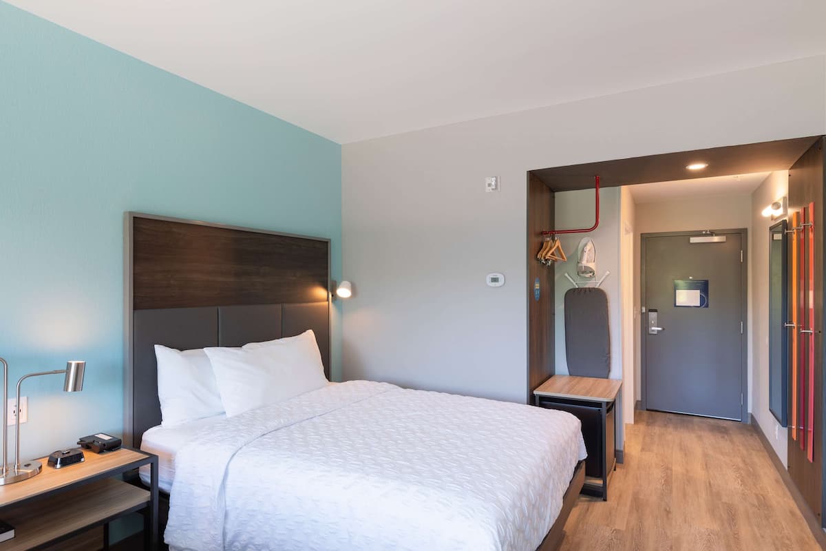 A hotel room with a bed, bedside table, lamp, and a door leading to another room.