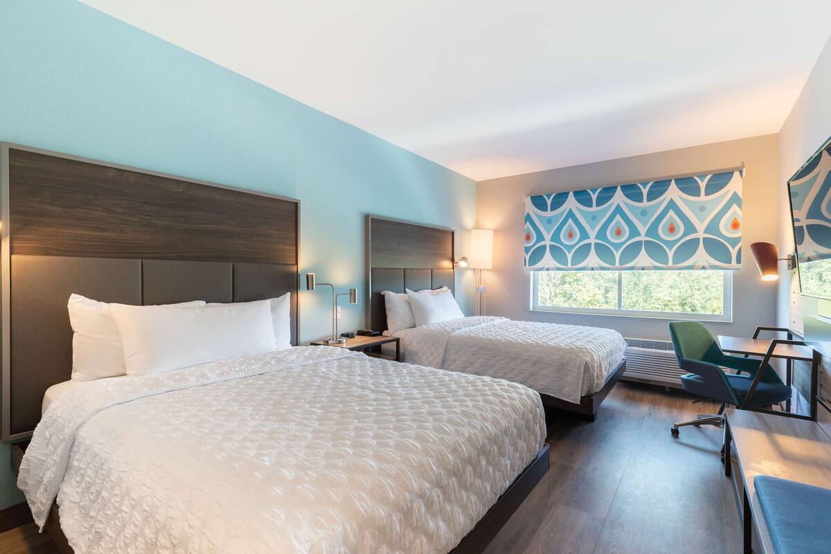A hotel room with two beds, a desk, and a chair.