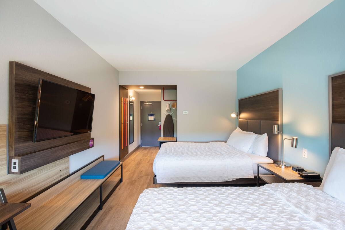 A hotel room with two beds, a TV, a desk, and a bench.