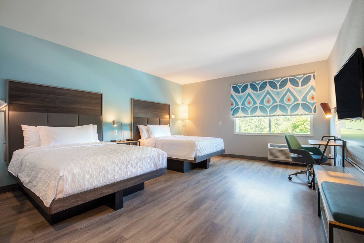 A hotel room with two beds, a desk, a chair, and a large window.