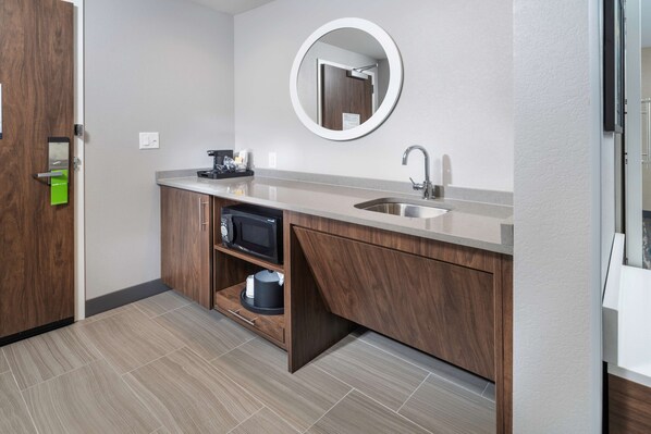 A modern bathroom with a wooden vanity, a sink, a mirror, and a microwave.