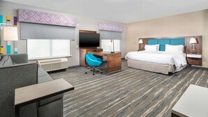 A hotel room with a bed, a desk with a chair, a TV, and a window with blinds.