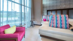 A modern hotel room with a large window, a sofa, a bed, and a small table.