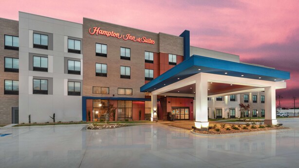 A Hampton Inn & Suites hotel with a modern facade, large windows, and a covered entrance area.