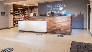 A reception desk with a "Welcome to the City of Colleges" sign, a Hilton logo, and a bookstore in the background. - Hampton Inn & Suites Conway (Conway)