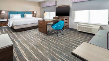 Ein Hotelzimmer mit Bett, Schreibtisch, Stuhl, Fernseher und großen Fenstern.