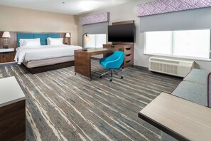 A hotel room with a bed, desk, chair, TV, and large windows.
