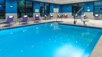 An indoor swimming pool with multiple lounge chairs and a lifeguard stand.