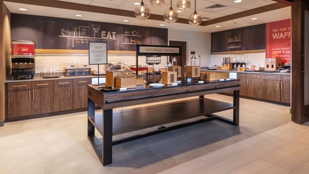 A modern breakfast area with a long counter, coffee machines, and a sign that reads "Happy Breakfast Starts Here". - Hampton Inn & Suites Conway (Conway)