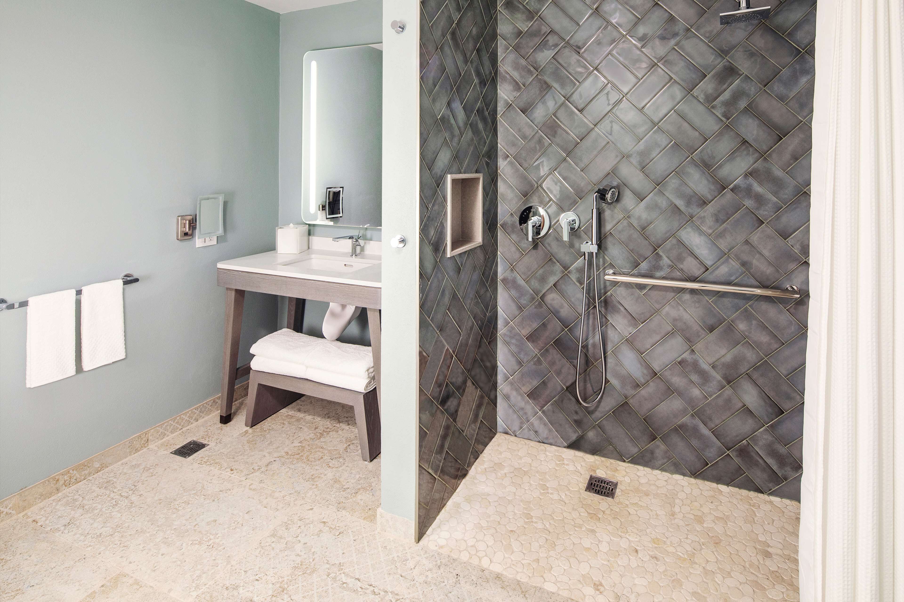 A modern bathroom with a vanity, a shower with a diamond-patterned wall, and a towel rack.