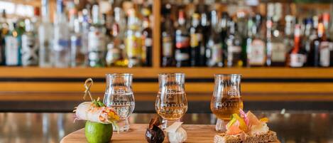 A bar counter with three glasses of liquor, a lime, and various garnishes.