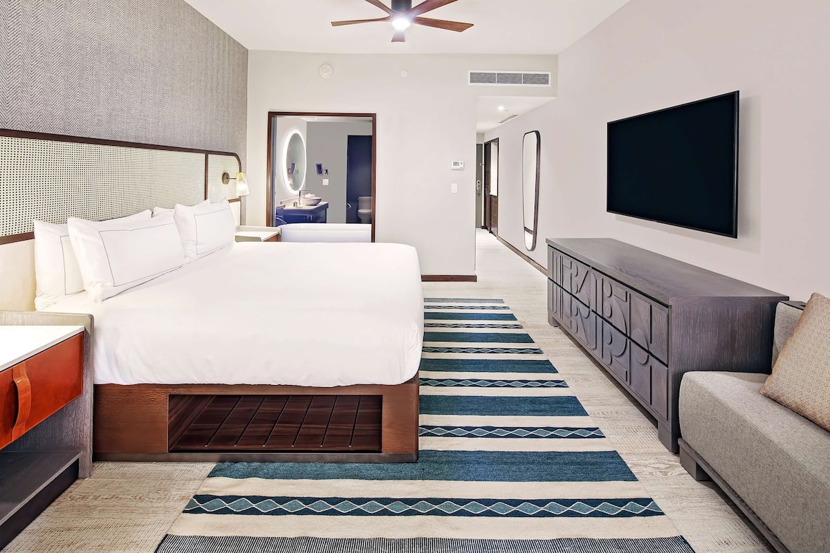 Habitación de hotel con una cama grande, un televisor montado en la pared, un sofá y una alfombra estampada.