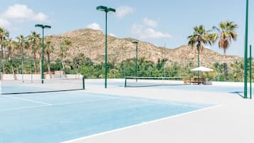 An outdoor tennis court with a net, benches, and palm trees.
