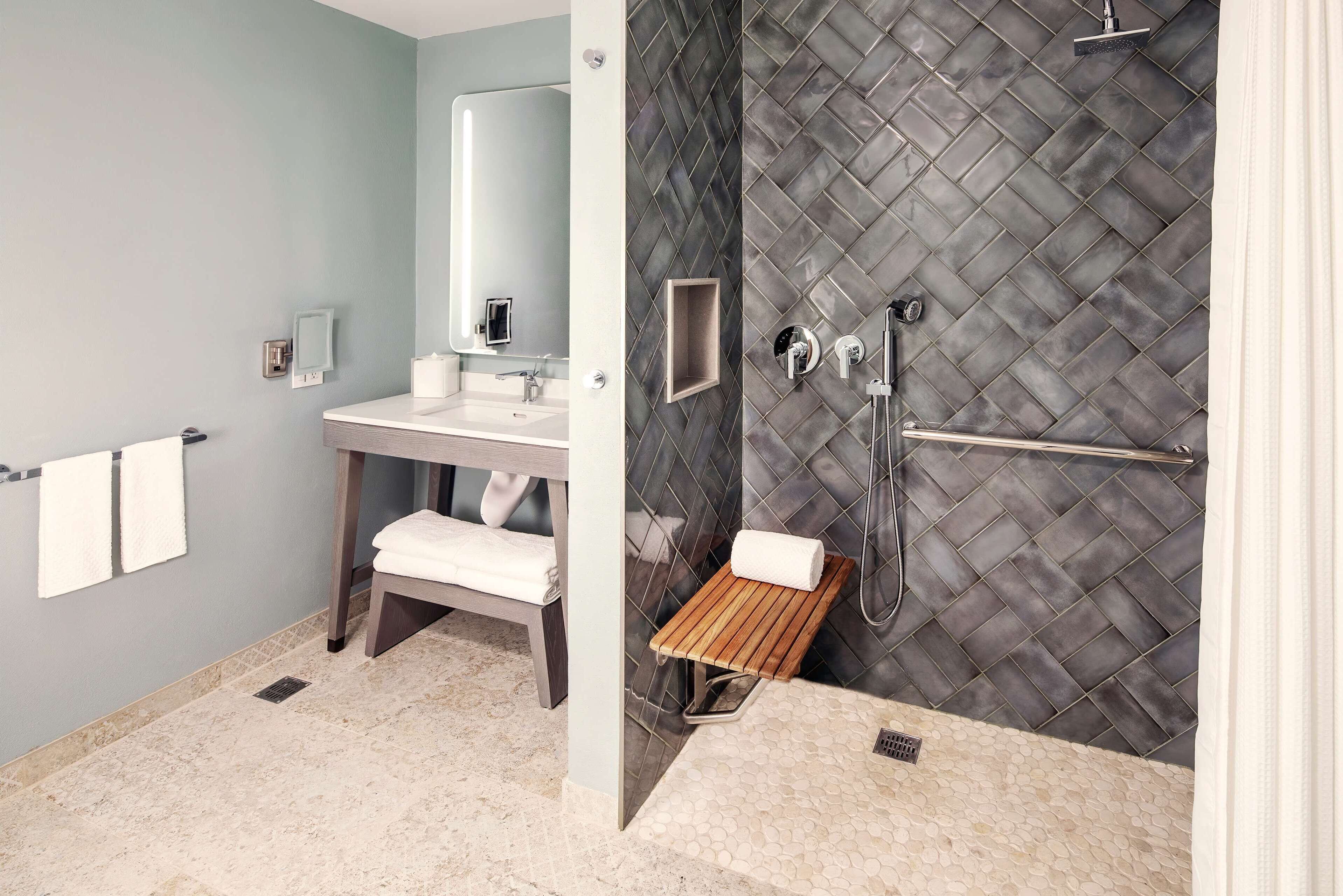 Un baño moderno con tocador, ducha con puerta de cristal y un banco.