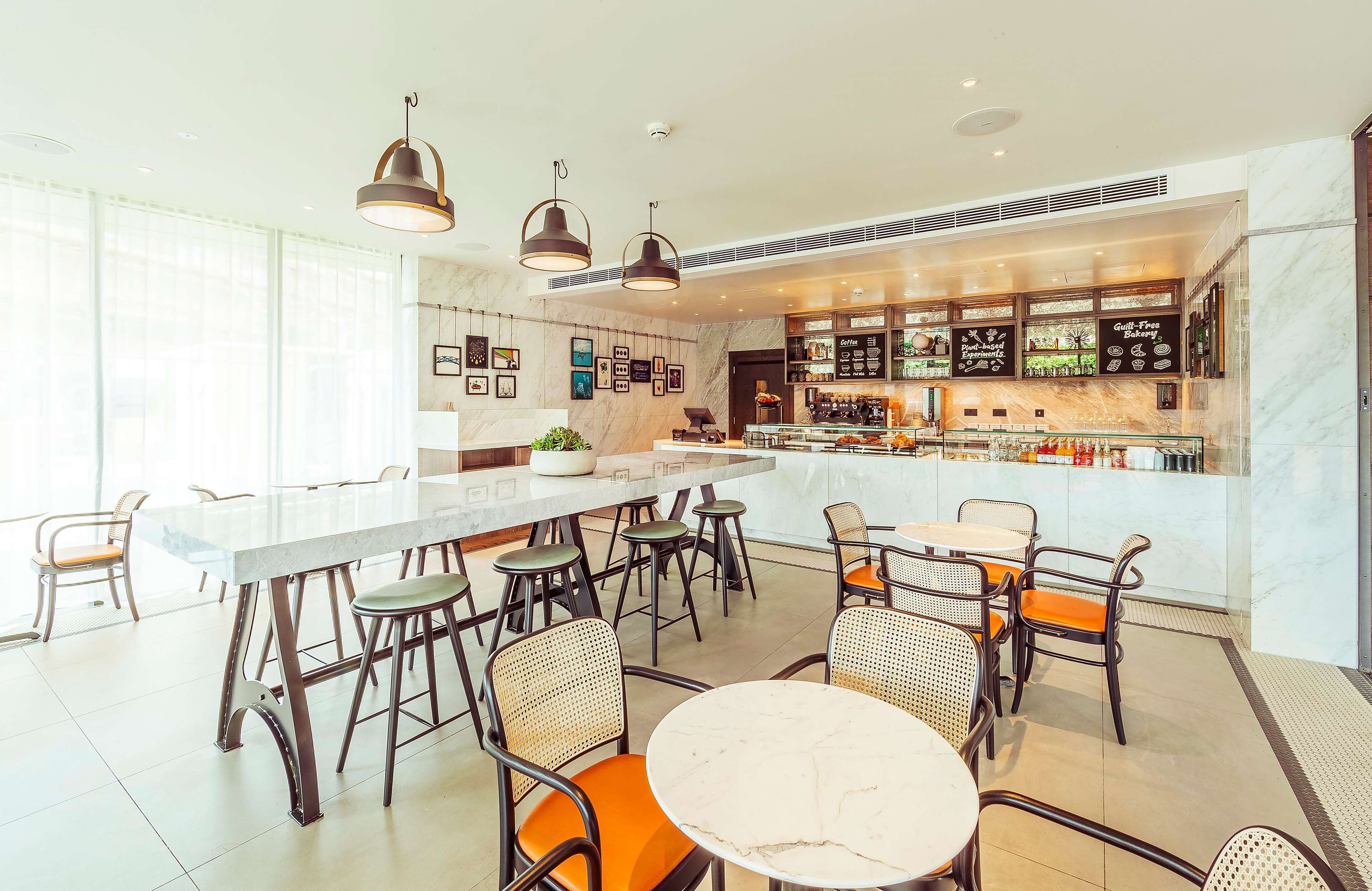 A modern cafe with a marble bar, wicker chairs, and pendant lighting.