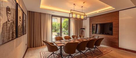 A modern conference room with a large table, comfortable chairs, a flat-screen TV, and a large window with curtains.