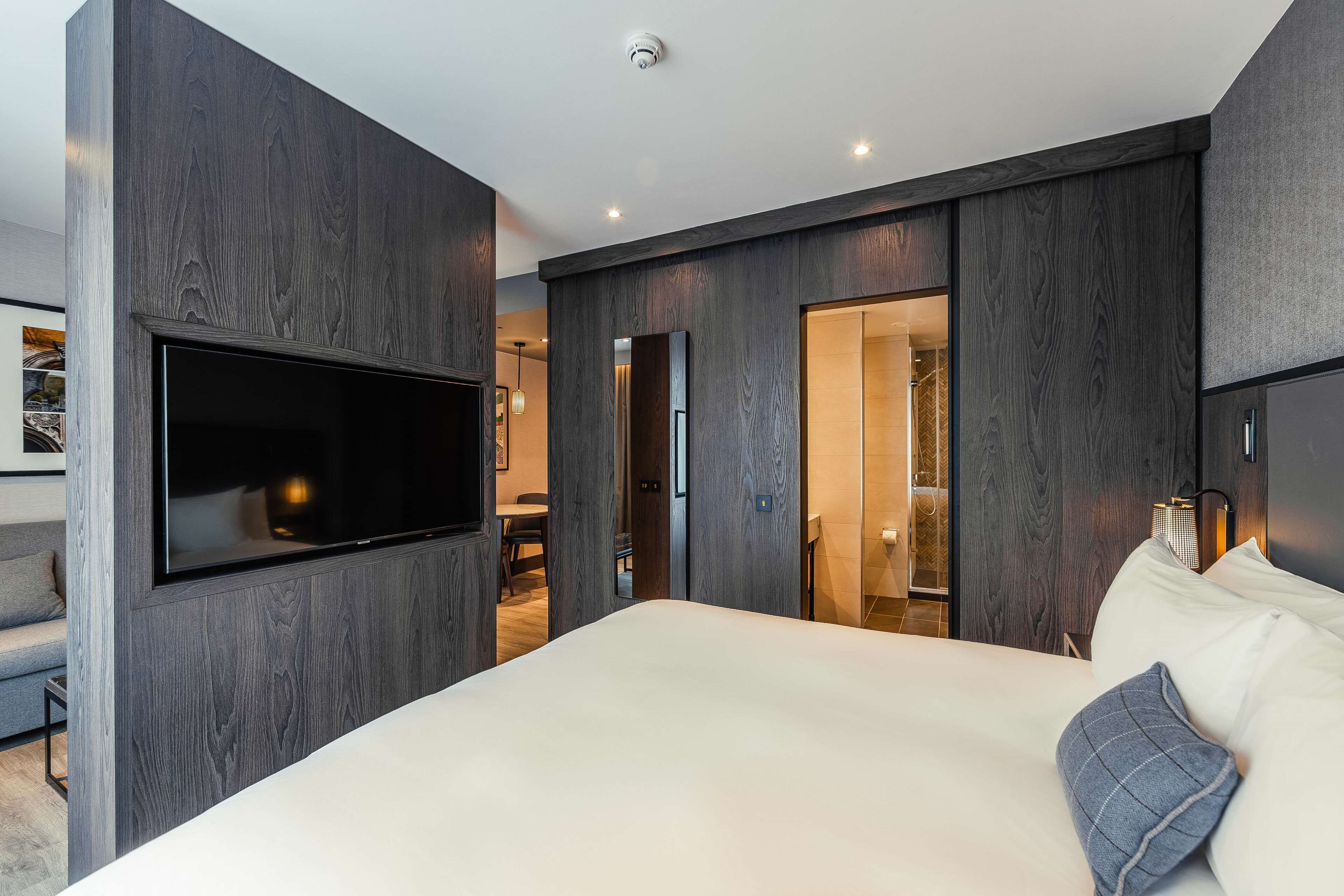A modern bedroom with a large bed, a mounted TV, and dark wood paneling.