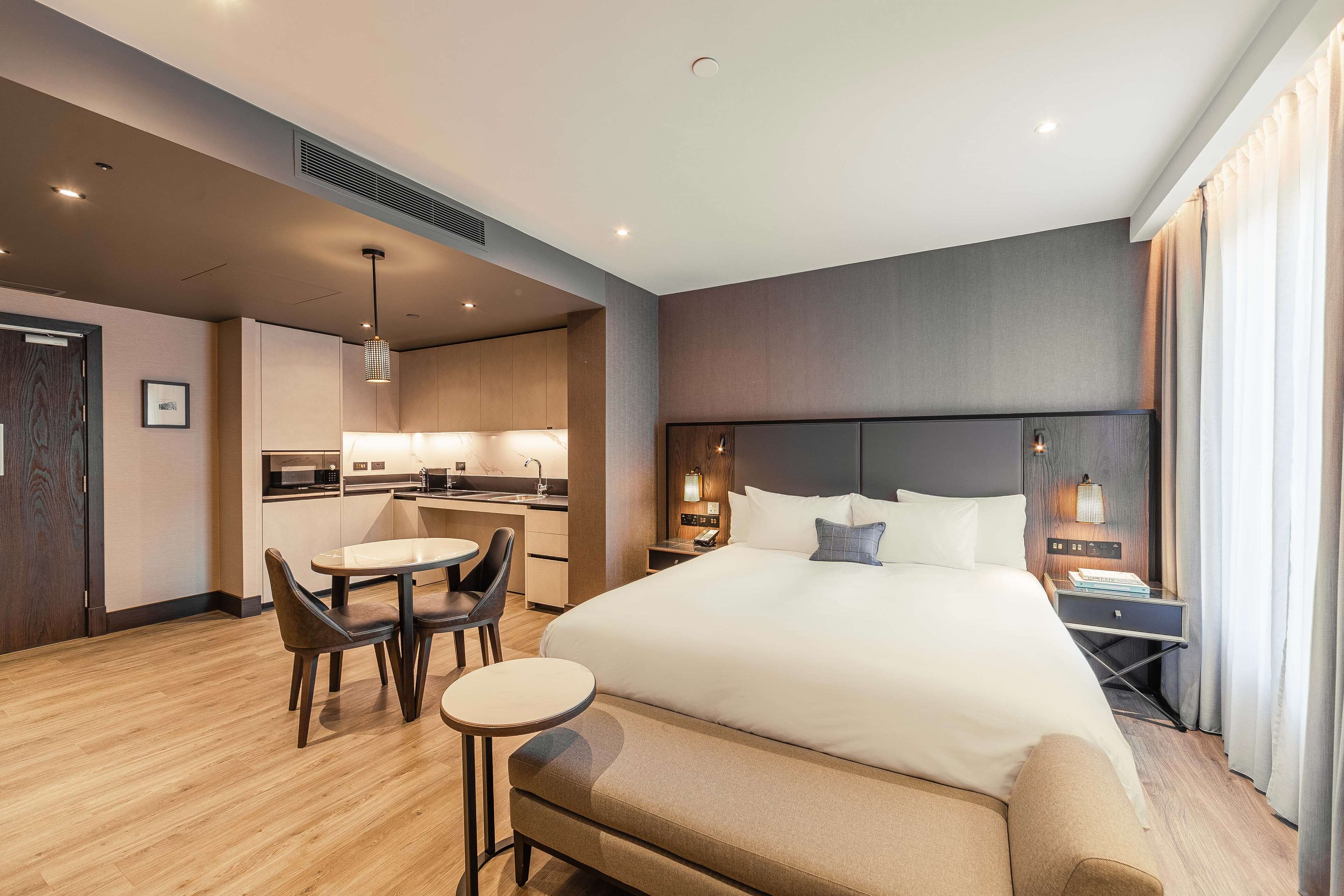 A hotel room with a large bed, a desk, a chair, a small table, and a sofa.