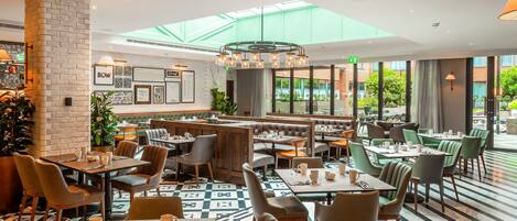 A modern restaurant with high ceilings, a skylight, and a mix of booth and table seating.