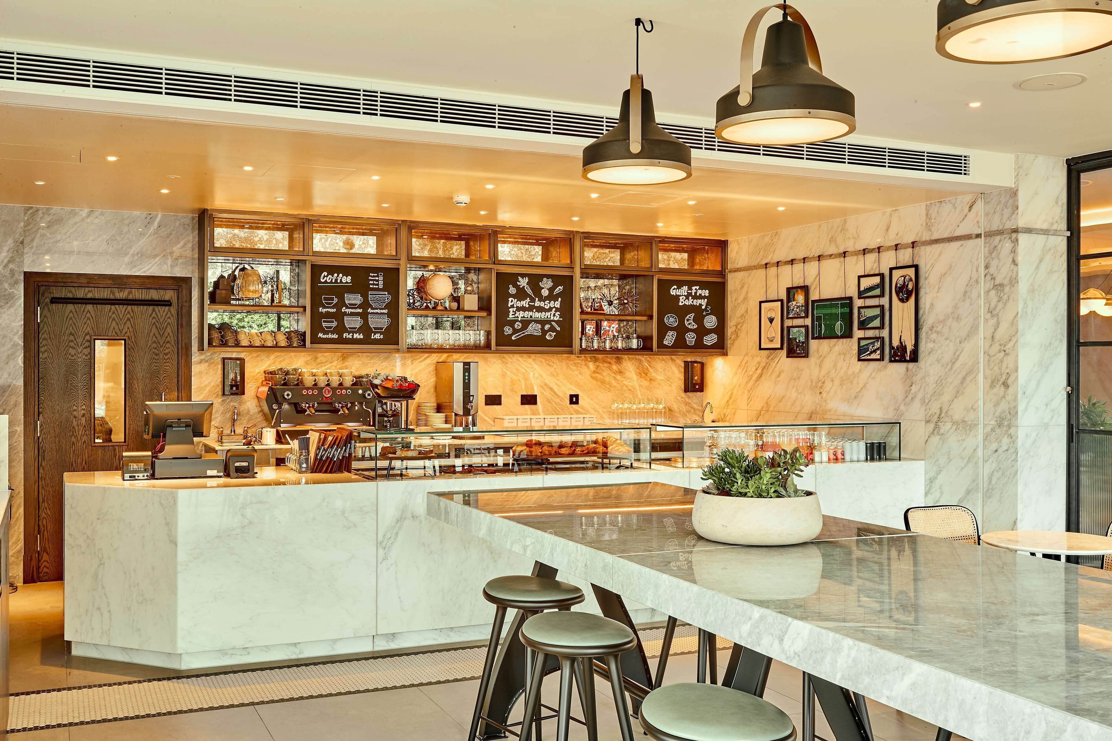 A modern bar area with a marble counter, stools, and overhead lighting.