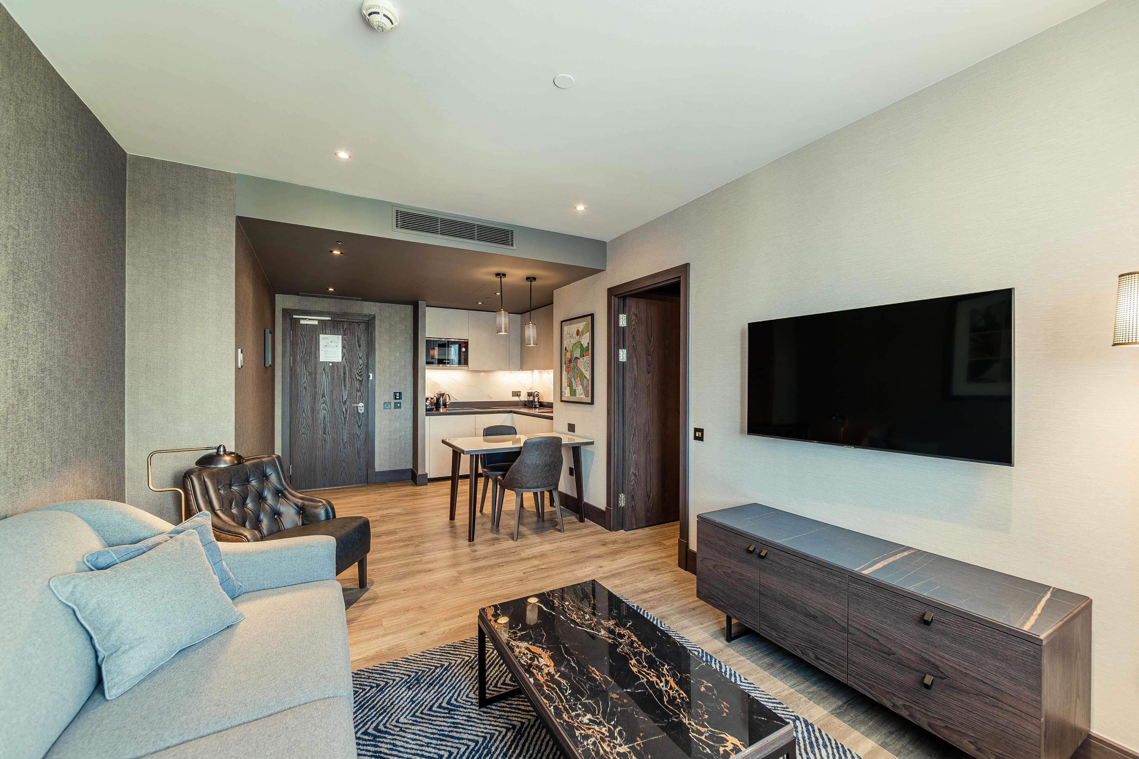 A modern living room with a sofa, a coffee table, a TV, and a dining area with chairs and a table.