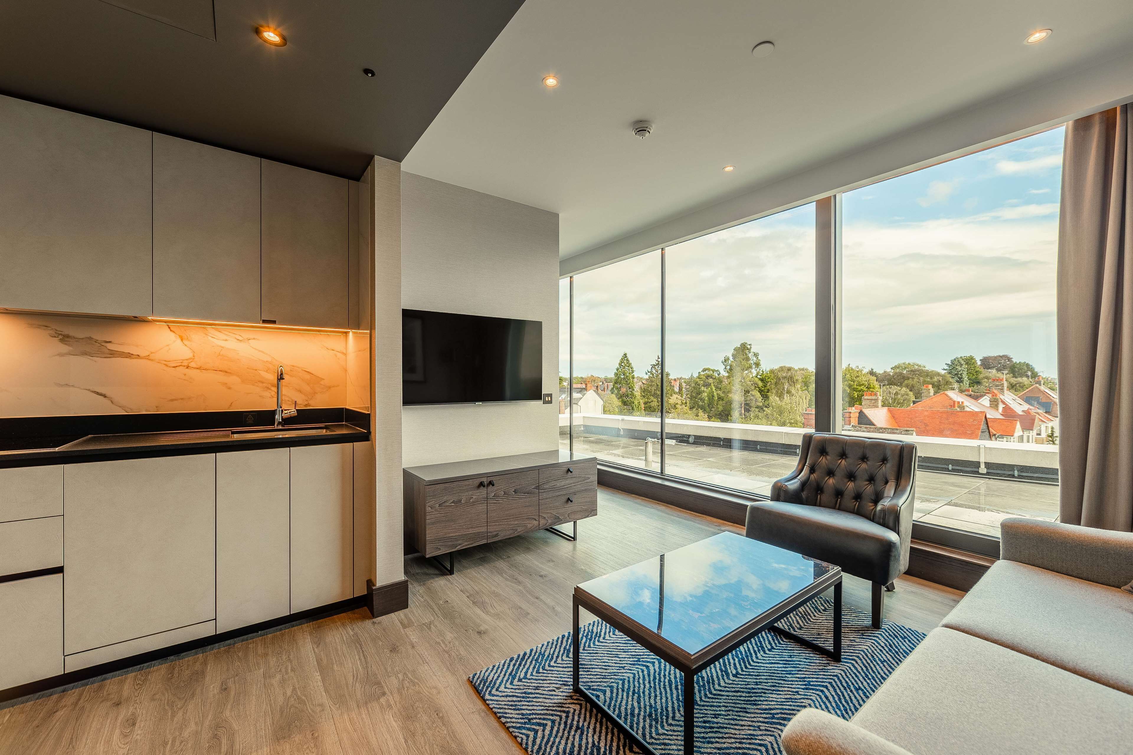 Ein moderner Wohnraum mit Küche, Flachbildfernseher, Sofa und großem Fenster mit Blick auf die Stadt.